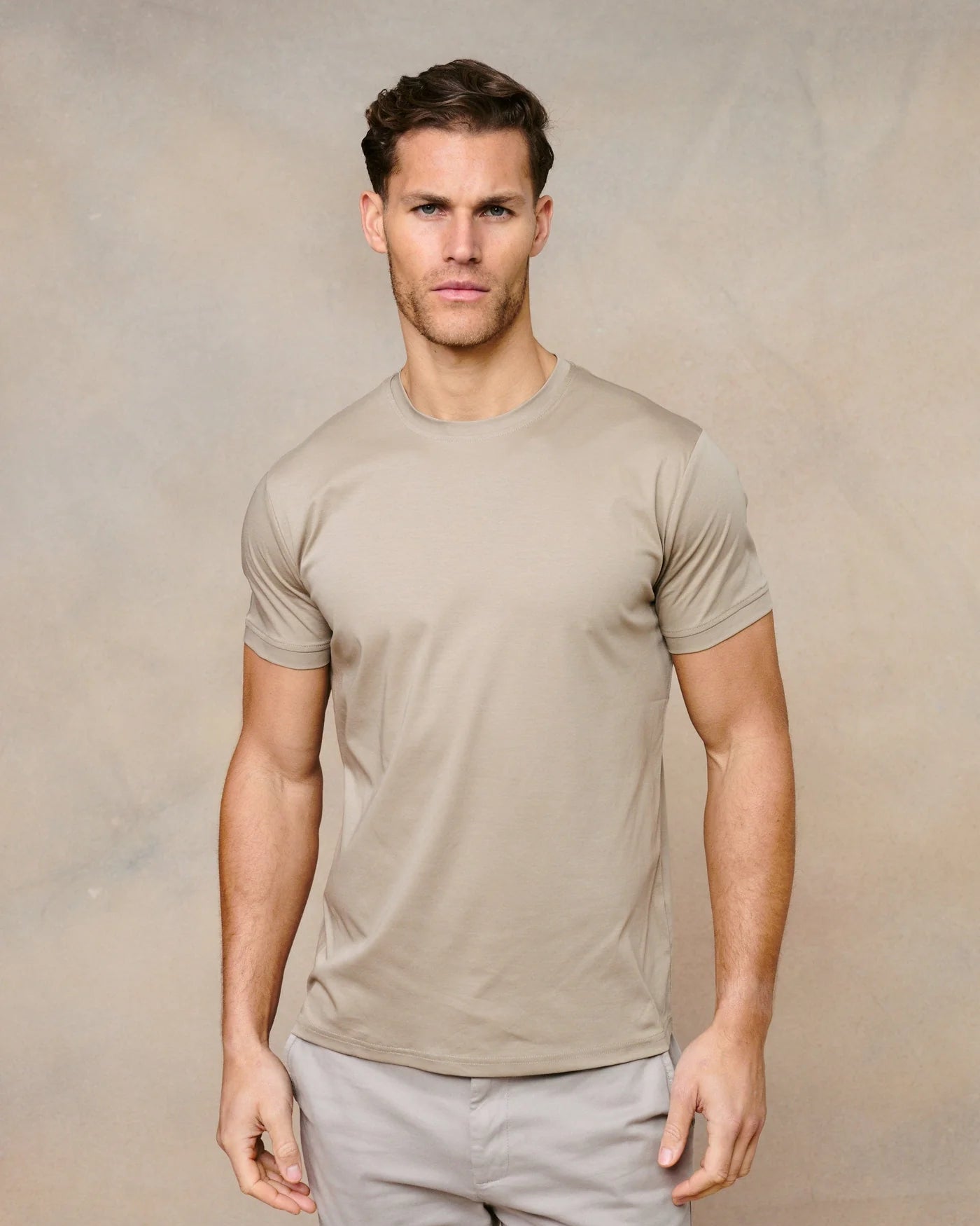 Man wearing a beige t-shirt and light gray pants against a beige background