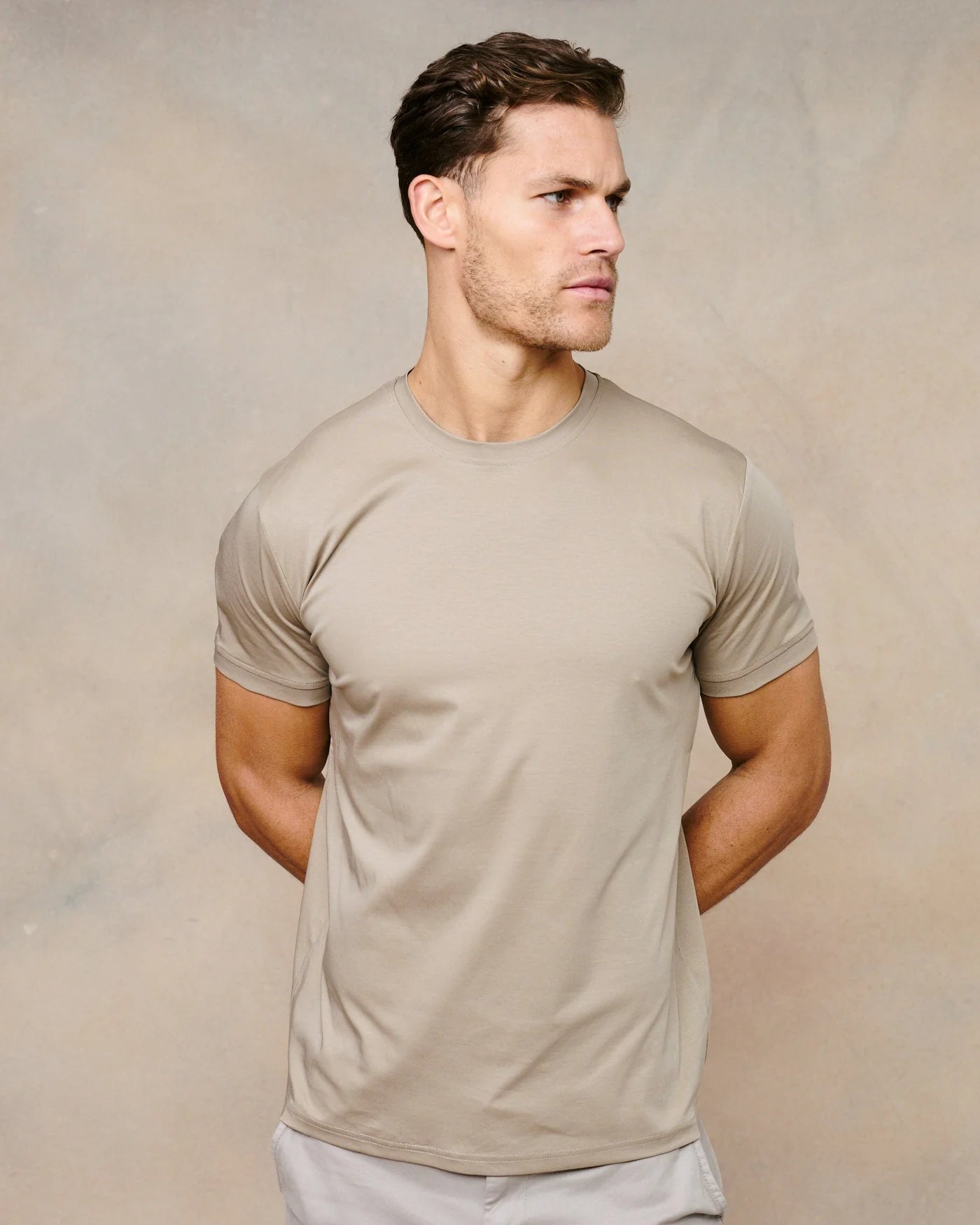 Man wearing a beige t-shirt and light gray pants against a beige background