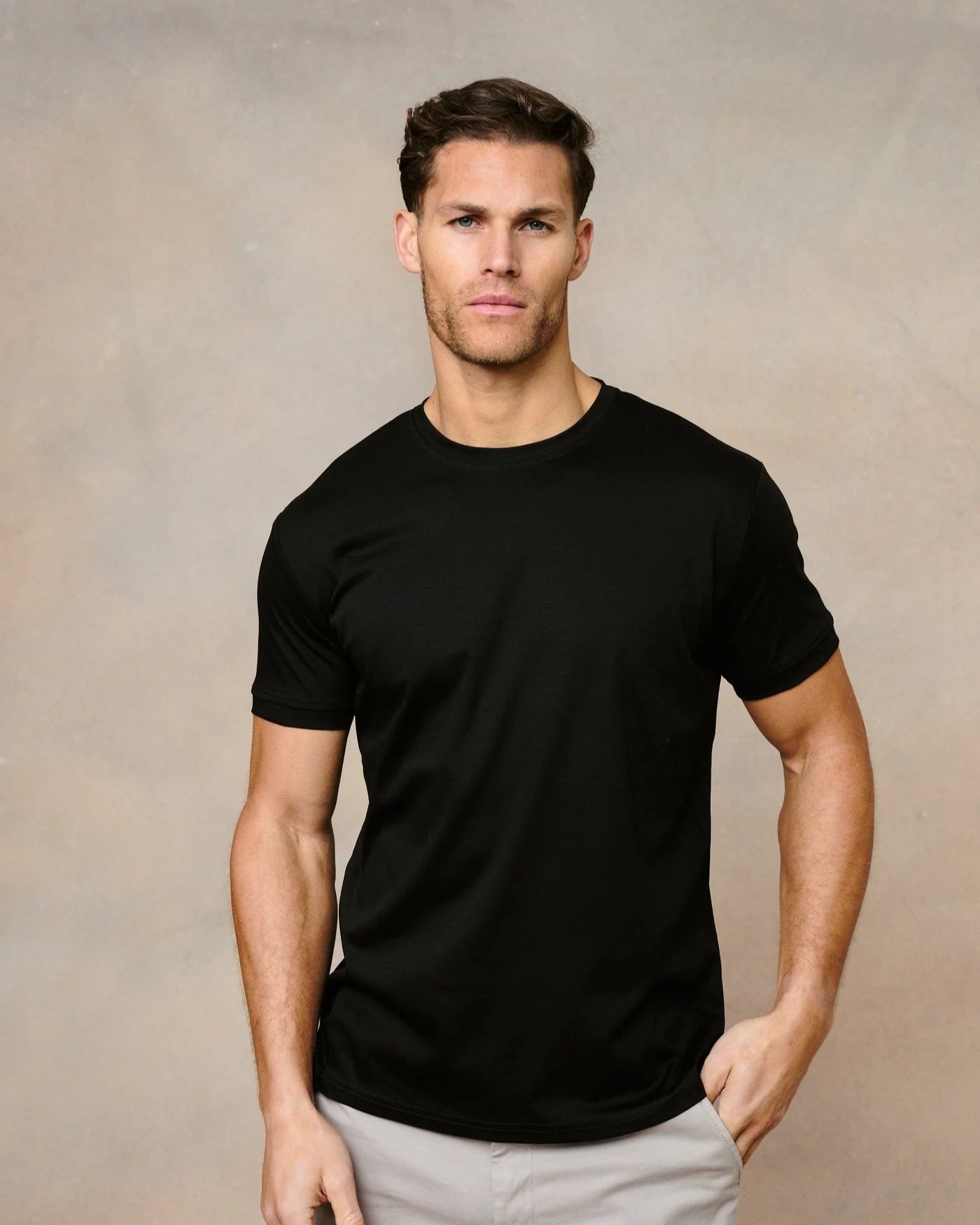 Man wearing a black t-shirt and light gray pants against a beige background