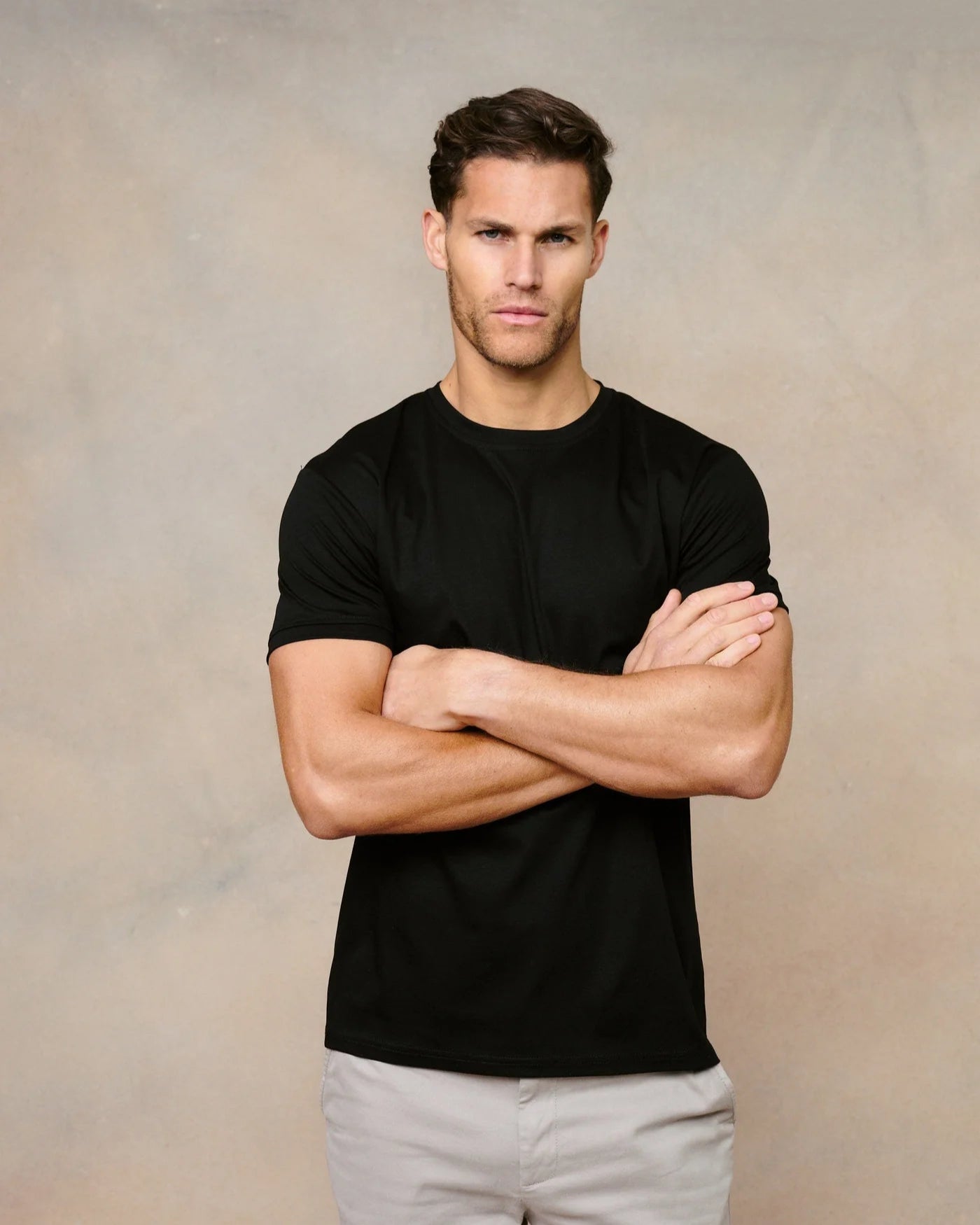 Man wearing a black t-shirt and light gray pants against a beige background