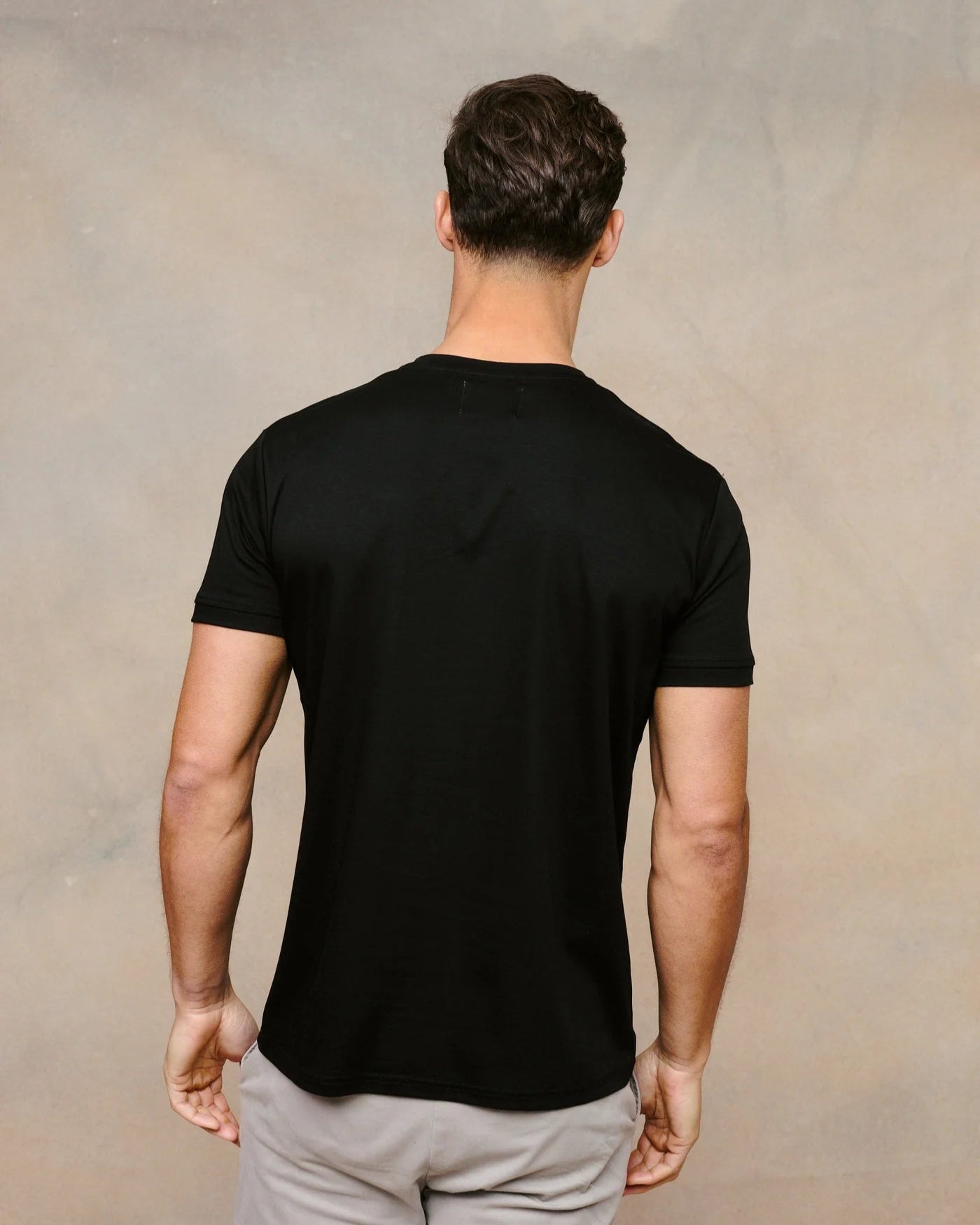 Man wearing a black t-shirt and light gray pants against a beige background