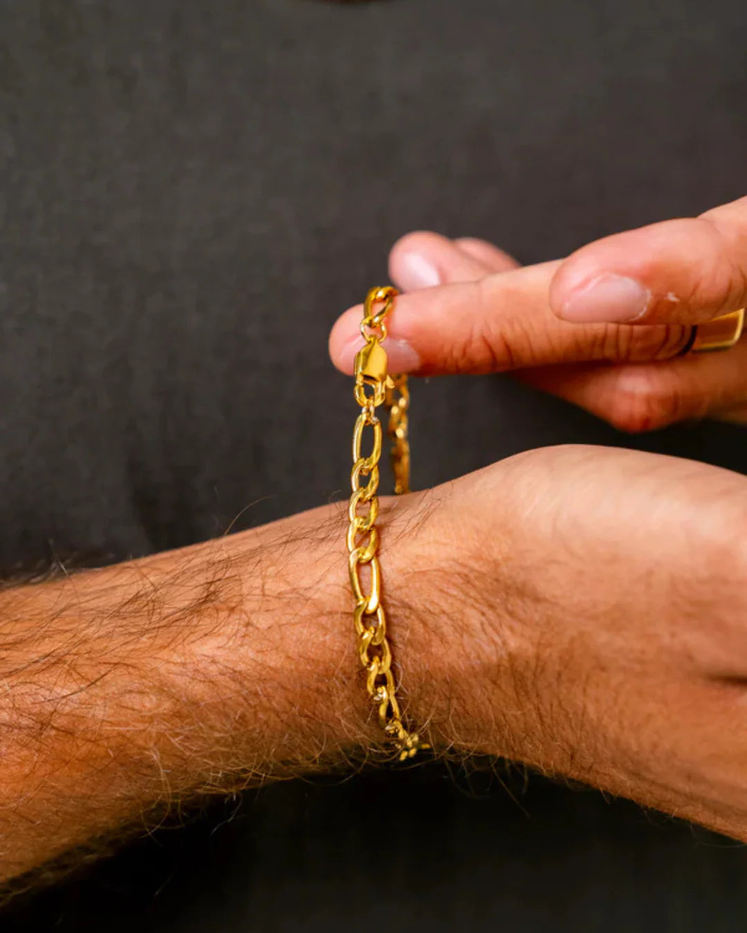 Gold chain bracelet being worn on a wrist with a dark background
