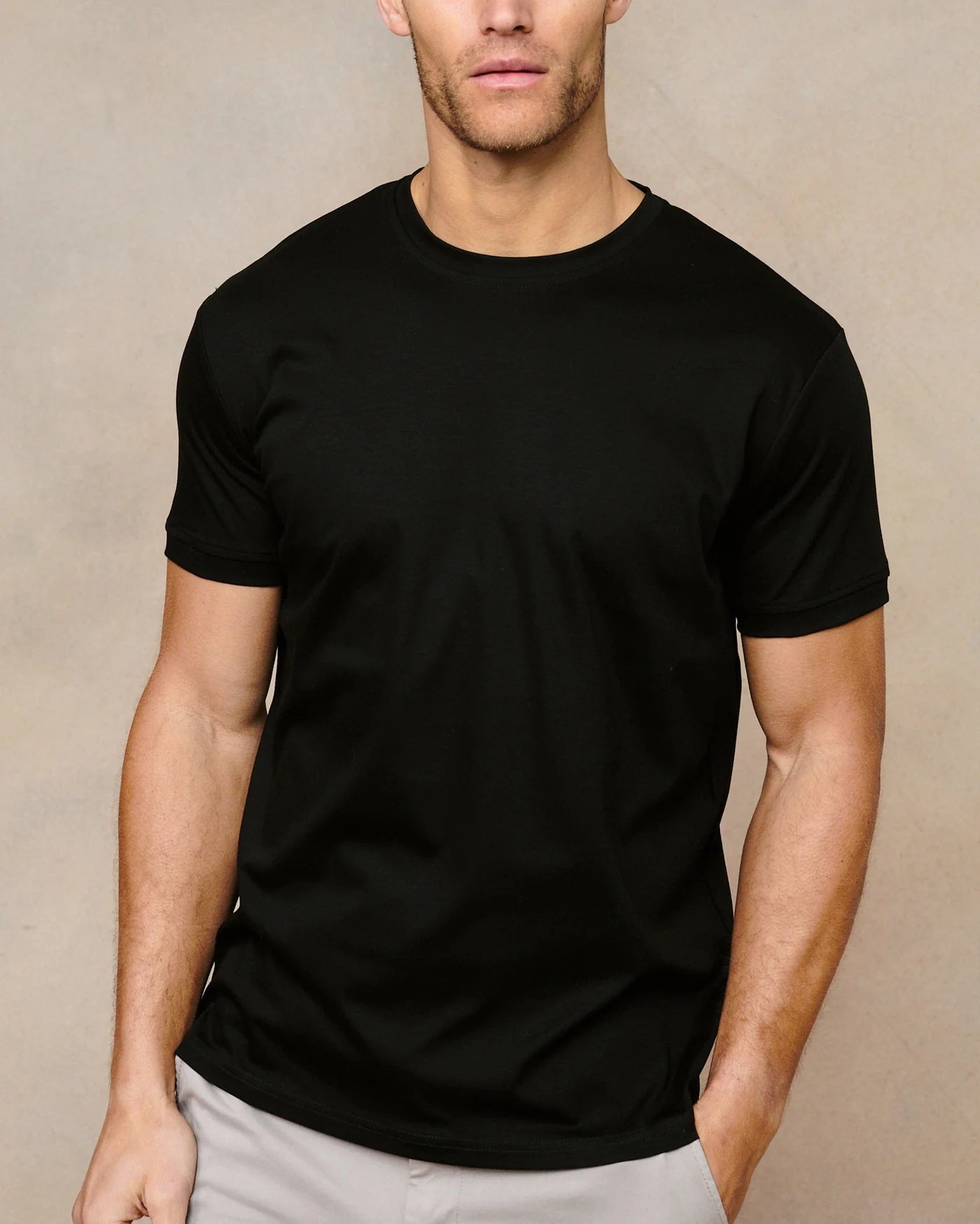 Man wearing a black t-shirt and light gray pants against a beige background