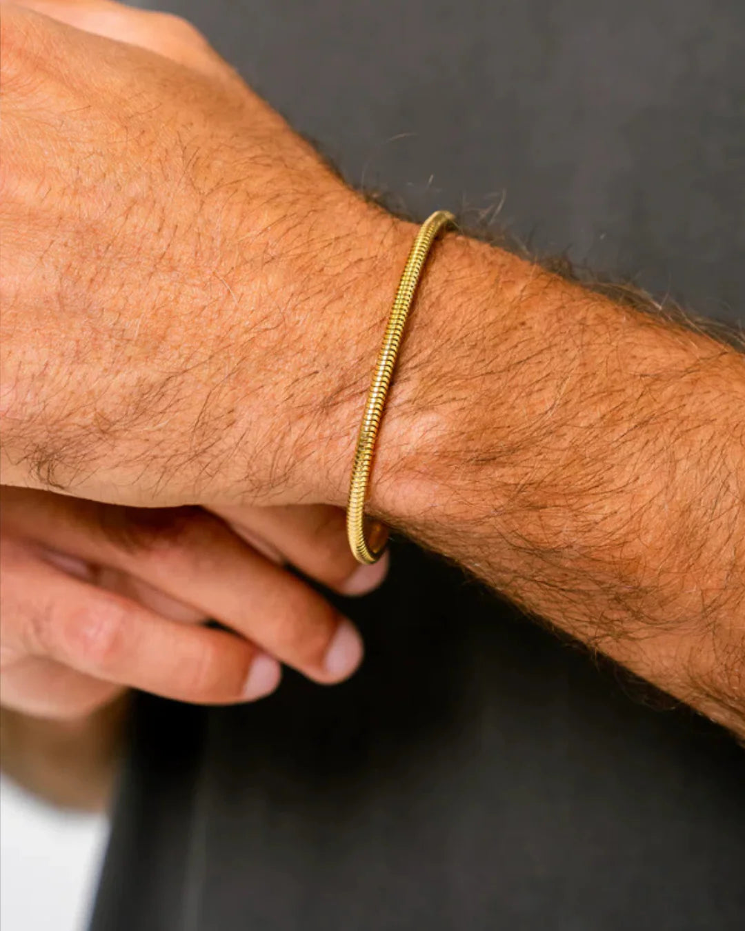 Gold bracelet on a person's wrist against a dark background