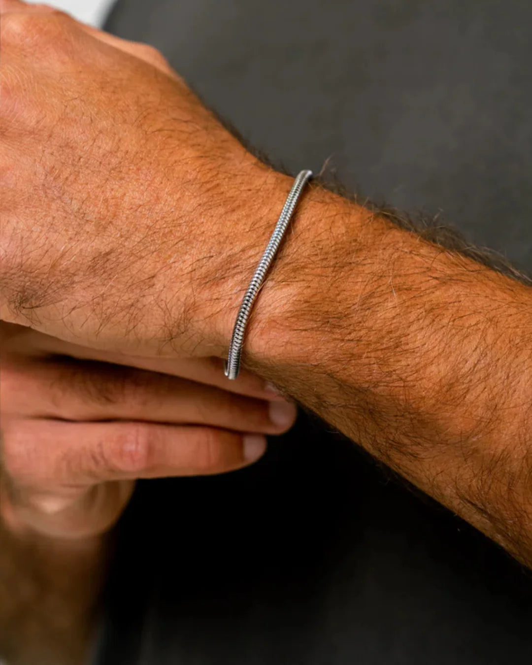 Close-up of a person's wrist wearing a silver bracelet against a dark background