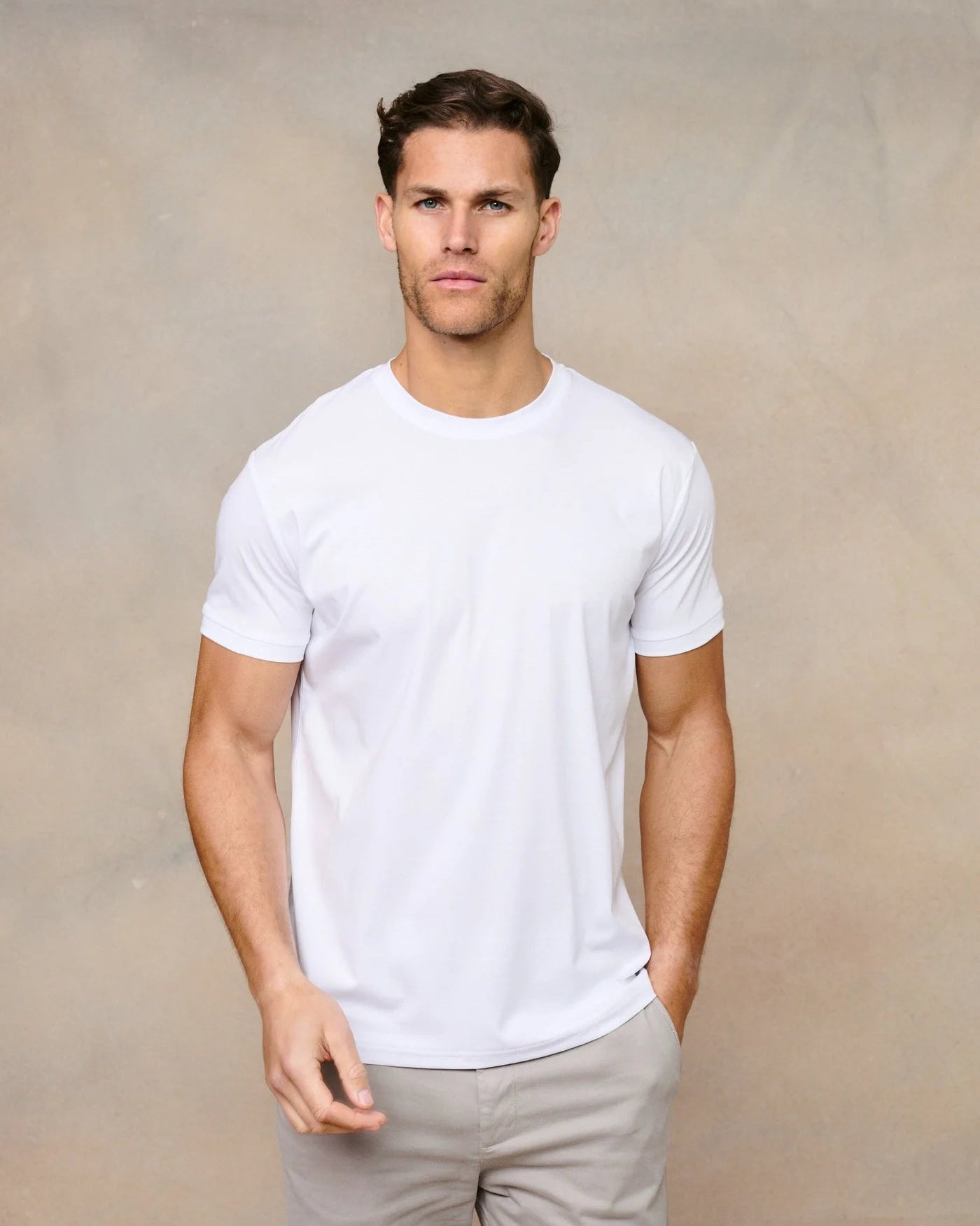 Man wearing a white t-shirt and light gray pants against a beige background