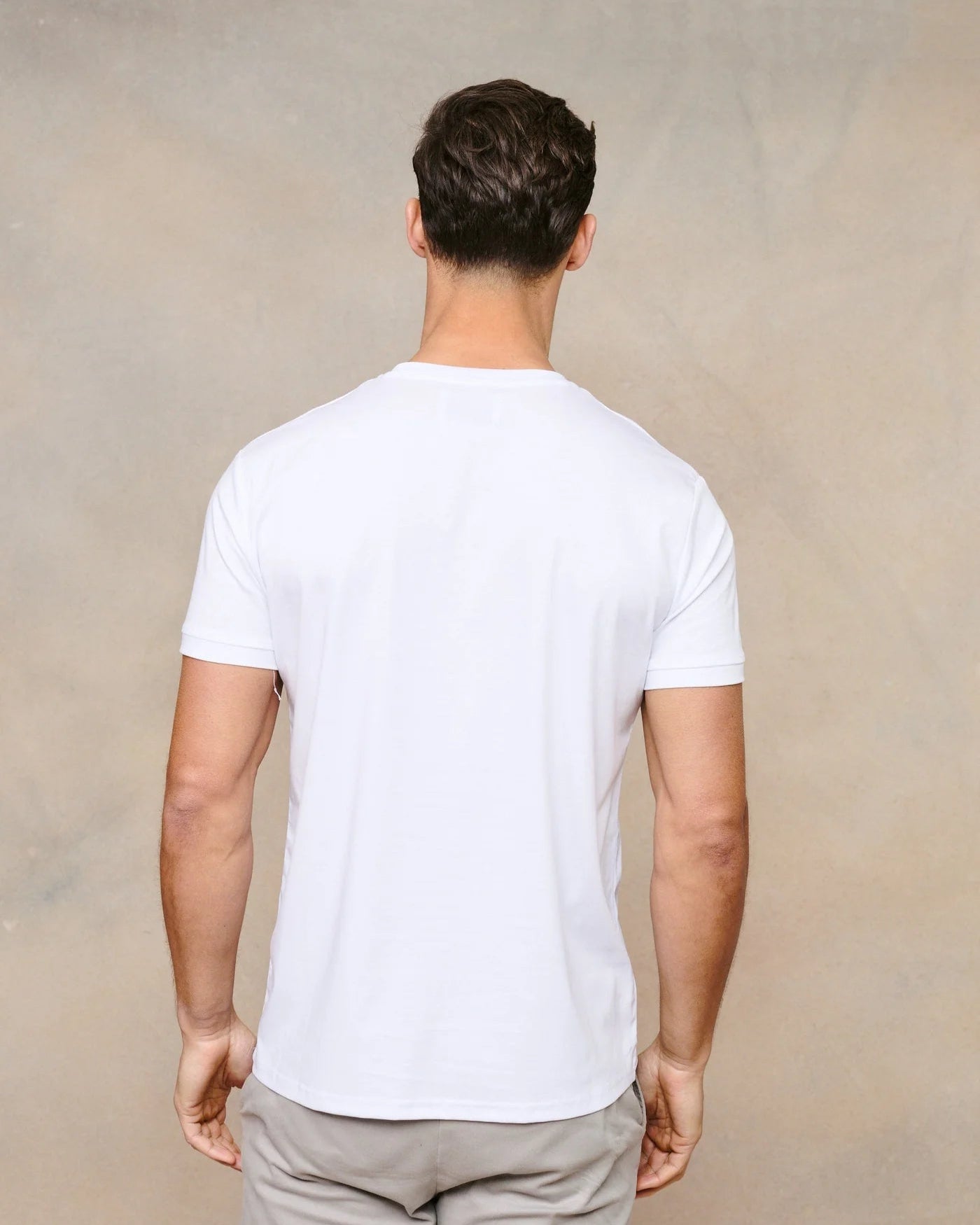 Man wearing a plain white t-shirt and light gray pants against a beige background