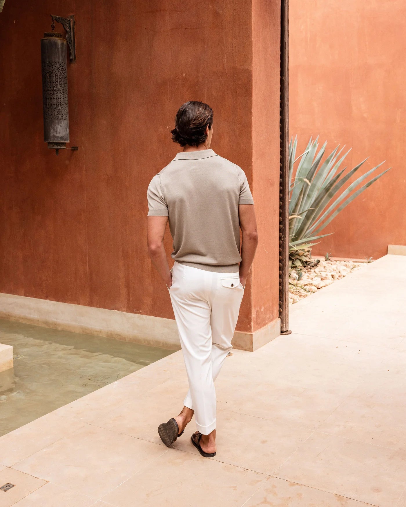Man walking along a path near a pool with a cactus plant in the background