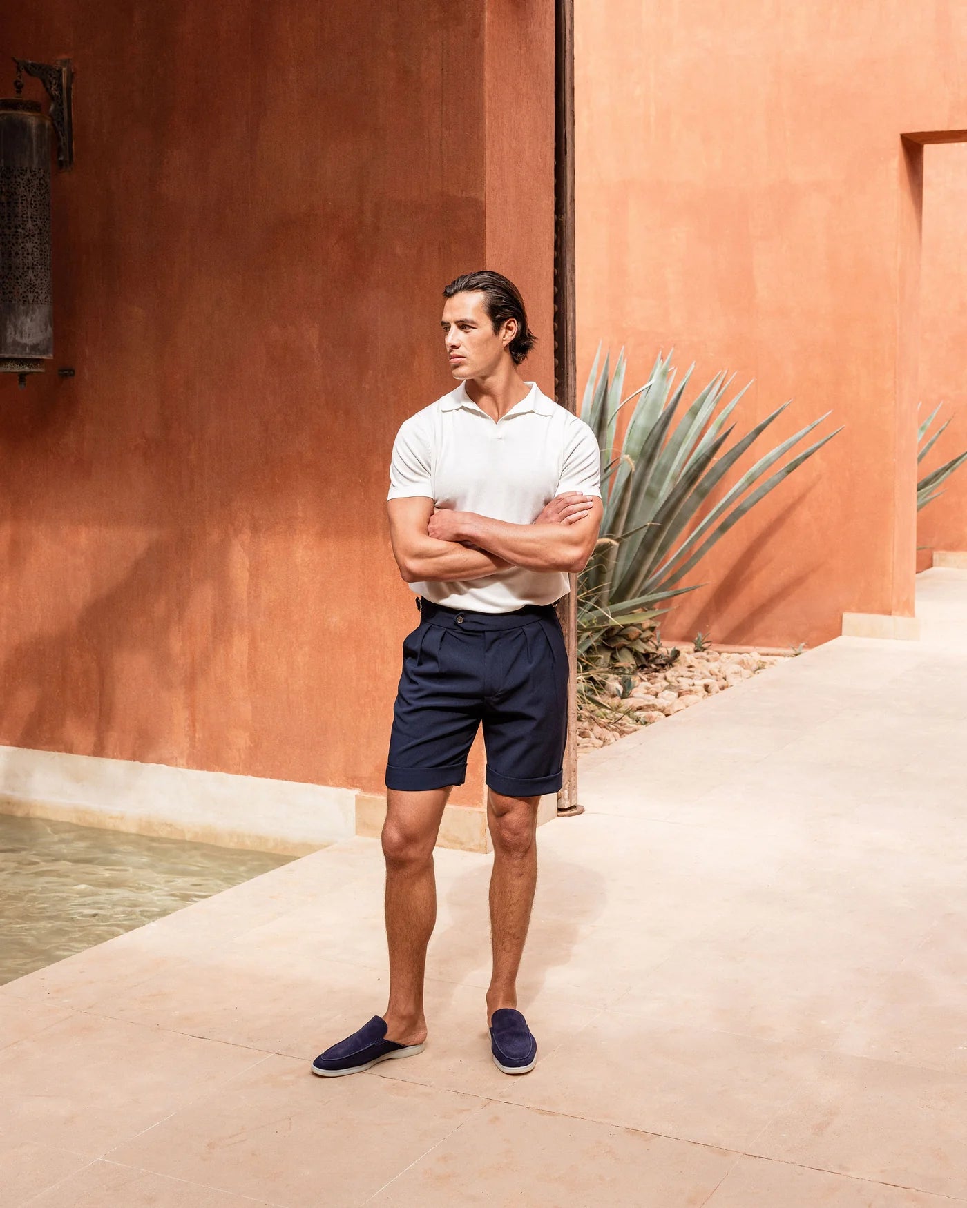 Man standing with arms crossed in front of a terracotta-colored wall with a plant.