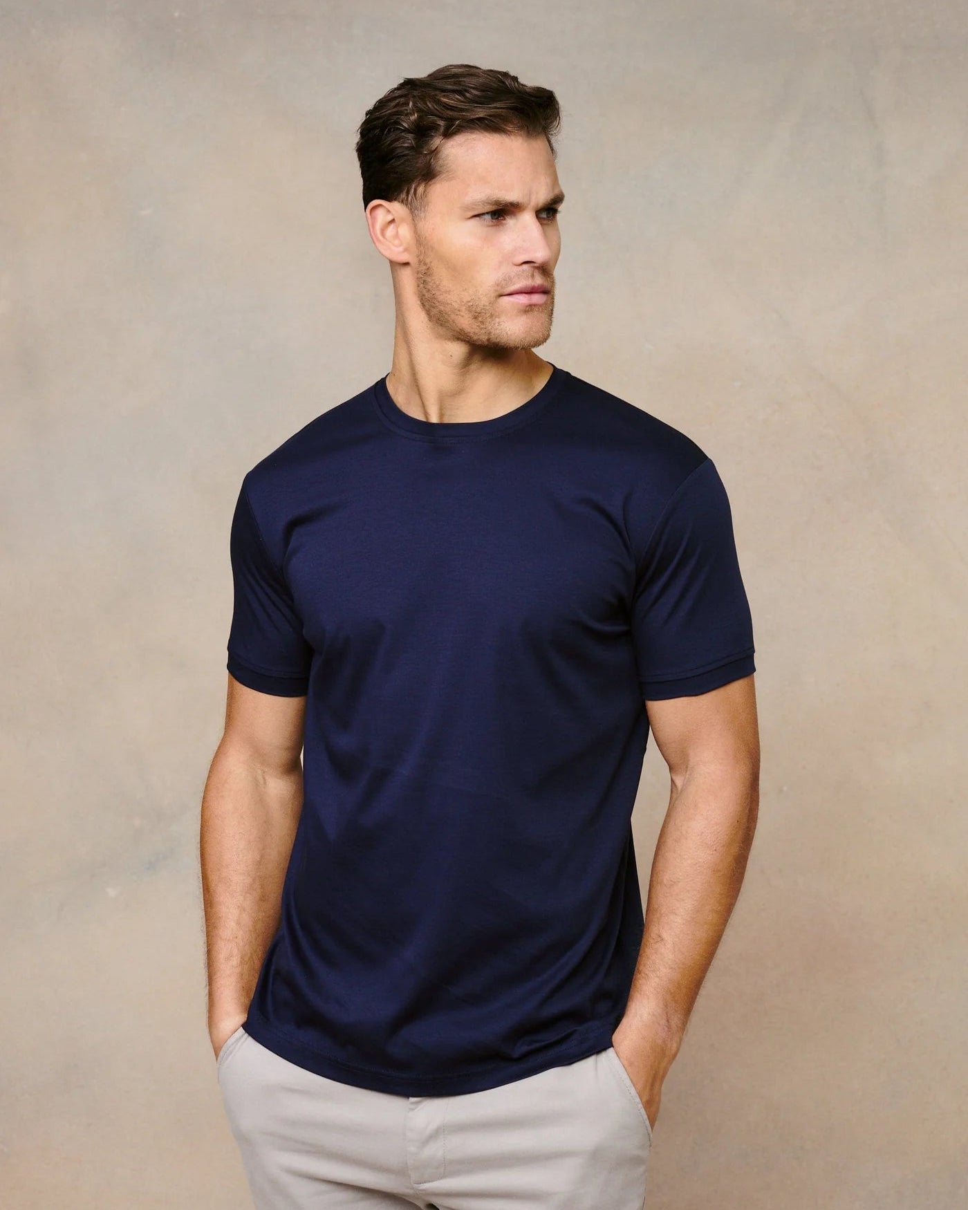 Man wearing a navy blue t-shirt and light gray pants against a beige background