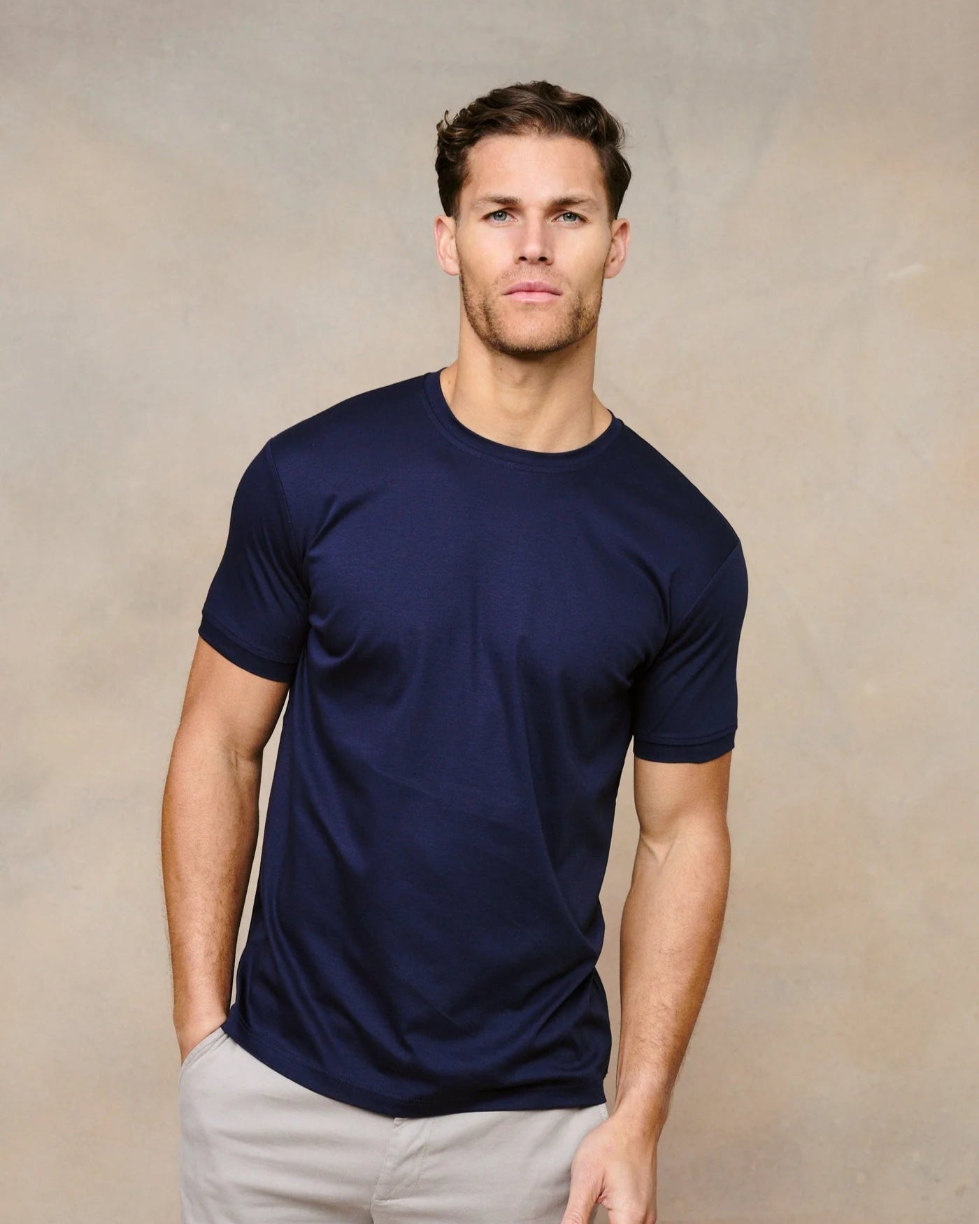 Man wearing a navy blue t-shirt and light gray pants against a beige background