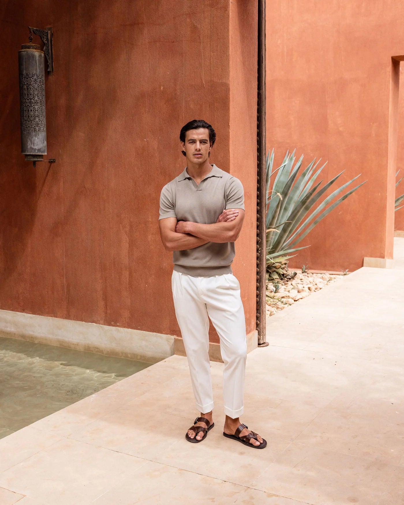 Man standing with arms crossed in front of a terracotta wall and cactus plant.