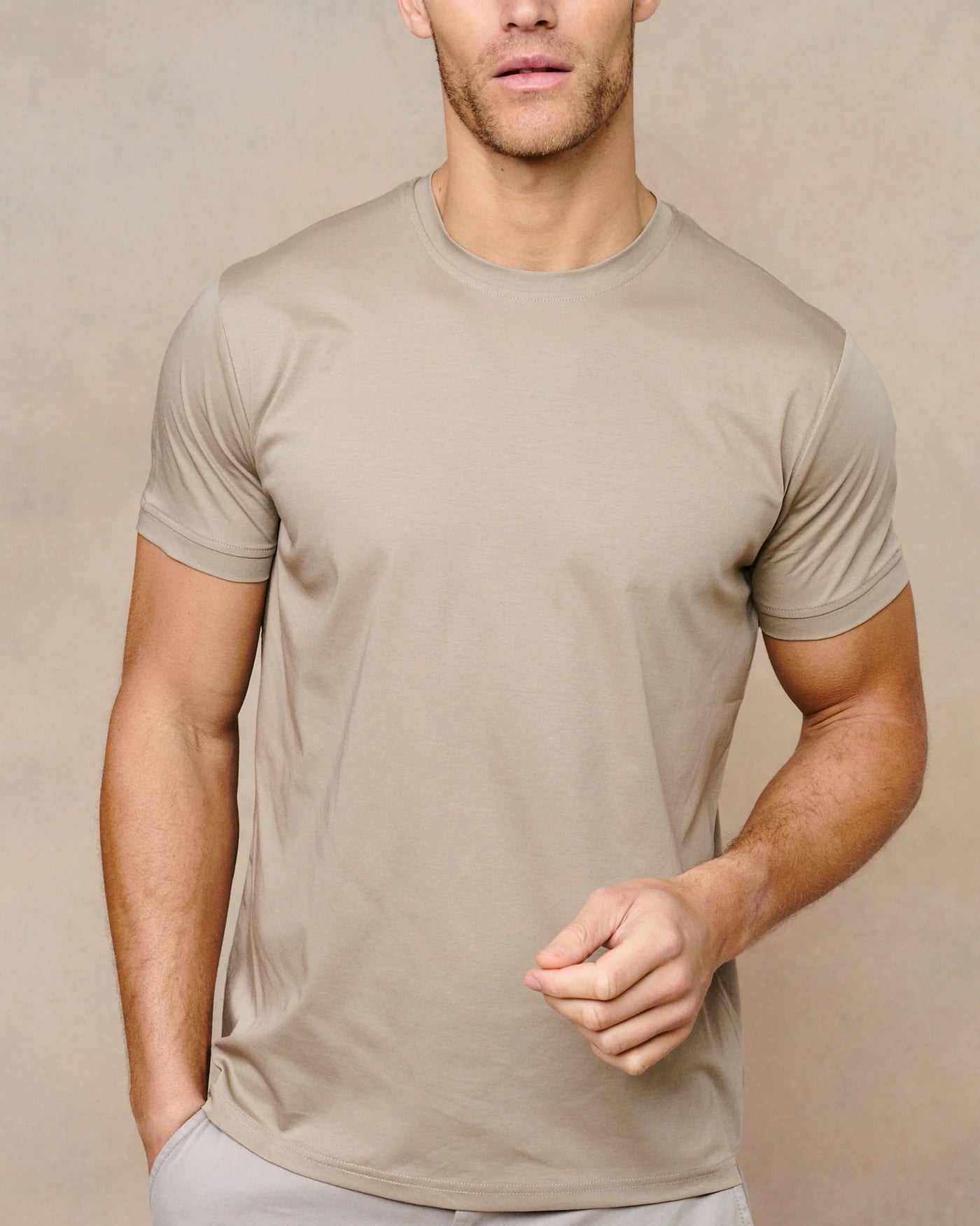 Man wearing a beige t-shirt and light gray pants against a beige background